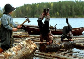 Lapsi ja kaksi aikuista rannassa tukkien keskellä.