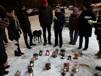 Ihmisiä kokoontuneena lyhtyjen ympärille talvimaisemassa.