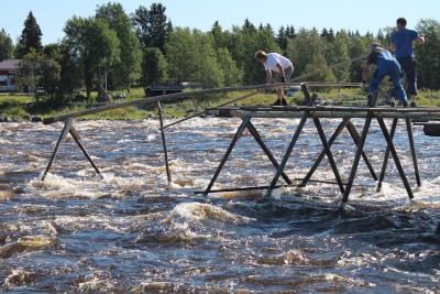 Kolme henkilöä rakentamassa siltaa veden virratessa sillan alla.