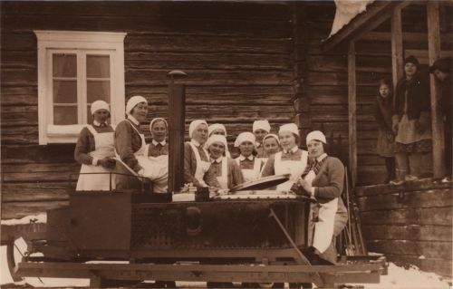 Muonittaja ryhmittyneenä suuren keittopadan ympärille. Oikealla kolme lasta.