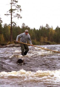 Henkilö laskemassa kuohuavaa koskea pitkin tukin päällä seisten.