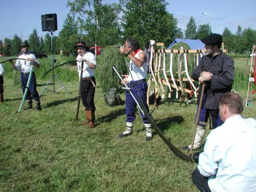 Viisi ihmistä seisoo viikatteet kädessä.