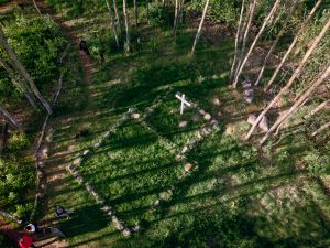 Metsän keskellä kirkon perustuksia mukaileva kivitys, ja keskellä valkoinen risti.