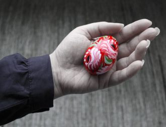 Vaaleanpunaisilla kukilla koristeltu punainen pääsiäismuna kämmenellä.
