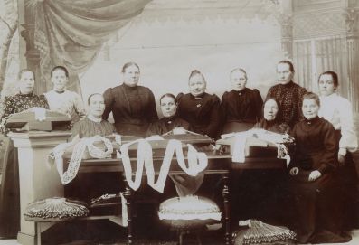 Kuvassa on 11 naista, joista neljä istuu alarivissä ja loput seisovat takarivissä. Kuva on otettu valokuvastudiossa 1900-luvun alkuvuosina. Kuvassa olevat naiset ovat pukeutuneet sen ajan asuihin, pitkiin hameisiin ja korkeakauluksisiin paitoihin. Kuvan etualalla on yhdeksän nypläystyynyä, joissa on kiinnitettynä keskeneräisiä pitsejä.