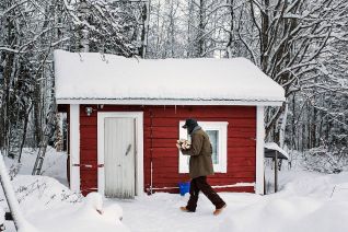 Talvinen valokuva, jossa henkilö kävelee puusaunaa kohti sylissään halkoja.