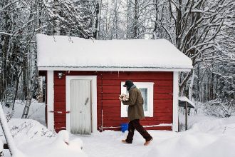 Person carrying wood to a wooden sauna in the winter.