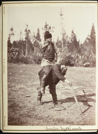 Mustavalkokuva miehestä istumassa toisen miehen selässä käsi ojossa.