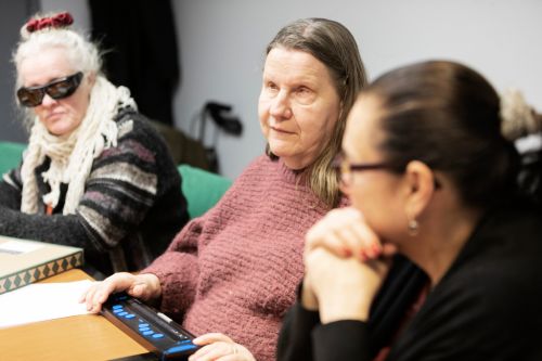 Alt-text: Tre kvinnor sitter vid ett bord. Framför kvinnan i mitten ligger en punktskriftsdisplay på bordet.