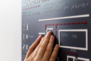 Henkilö tutkii käsillään Hätäpoistumistie-kohokarttaa, jossa on myös pistekirjoitusta.