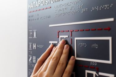 Henkilö tutkii käsillään Hätäpoistumistie-kohokarttaa, jossa on myös pistekirjoitusta.