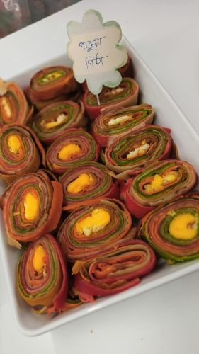 Lautasellinen bangladeshilaisia leivonnaisia, jotka koostuvat rullatusta värikkäästä taikinasta.