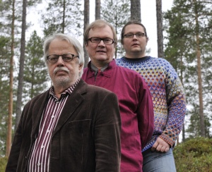 The members of the band are standing in the woods and posing at the camera.