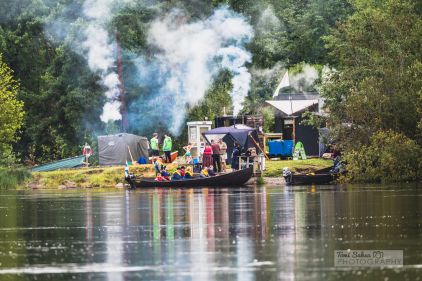 Metsäinen ranta, jolle on pystytetty useita saunoja. Joukko ihmisiä saunoo saunoissa.