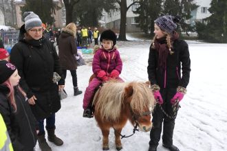 Pieni lapsi ratsastamalla ponilla, jota aikuinen taluttaa.