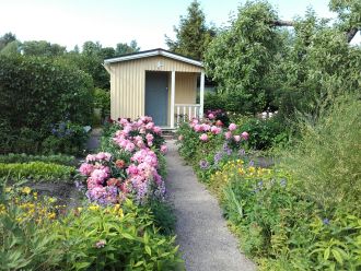Polku keltaiselle mökille, polun ympärillä vaaleanpunaisia kukkia.