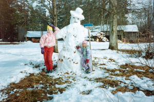 Small children posing next to a snowman.