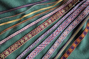 Kuvassa on värikkäitä lautanauhoja aseteltuna vihreän kankaan päälle. Nauhat on kudottu Suomen rautakauden mallien mukaan. Kuva: Mervi Pasanen