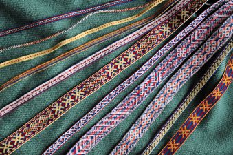 Kuvassa on värikkäitä lautanauhoja aseteltuna vihreän kankaan päälle. Nauhat on kudottu Suomen rautakauden mallien mukaan. Kuva: Mervi Pasanen
