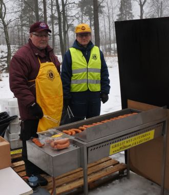 Kaksi henkilöä paistamassa makkaraa grillissä.